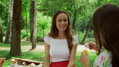 woman laughing together with children in park. happy kids blowing soap bubbles