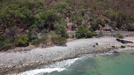 movimiento aéreo de drones hacia los automóviles que conducen a lo largo de una carretera junto al agua azul tropical