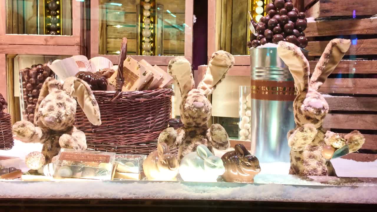 Cute animatronic rabbits moving in a festive Christmas window display. Decorated with chocolates, baskets, and fake snow, this holiday scene attracts shoppers and children