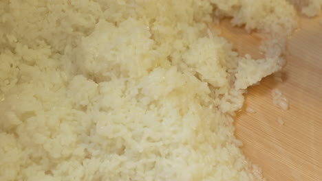 mixing japanese white rice moistened with vinegar mixture into the wooden basin in the kitchen
