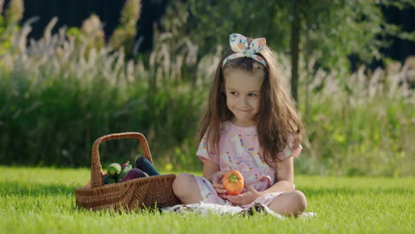 happy child is sitting on the lawn near a basket of vegetables. picnic concept