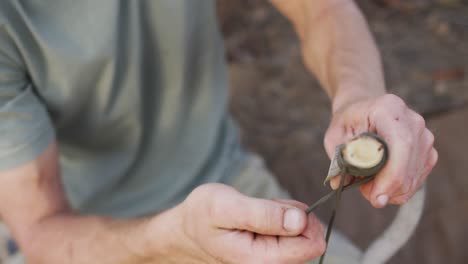 Caucasian-male-survivalist-securing-cord-to-branch-to-make-a-fire-bow-at-camp-in-wilderness