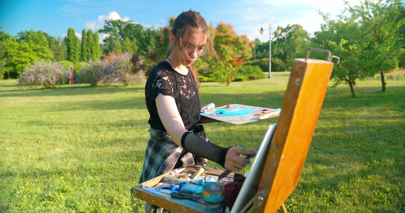 Young Woman Painting on an Easel Outdoors in a Sunny Park