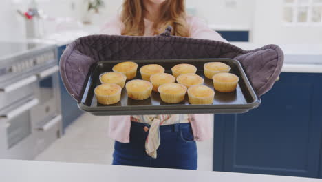 portrait of proud teenage girl taking out tray of homemade cupcakes from the oven at home