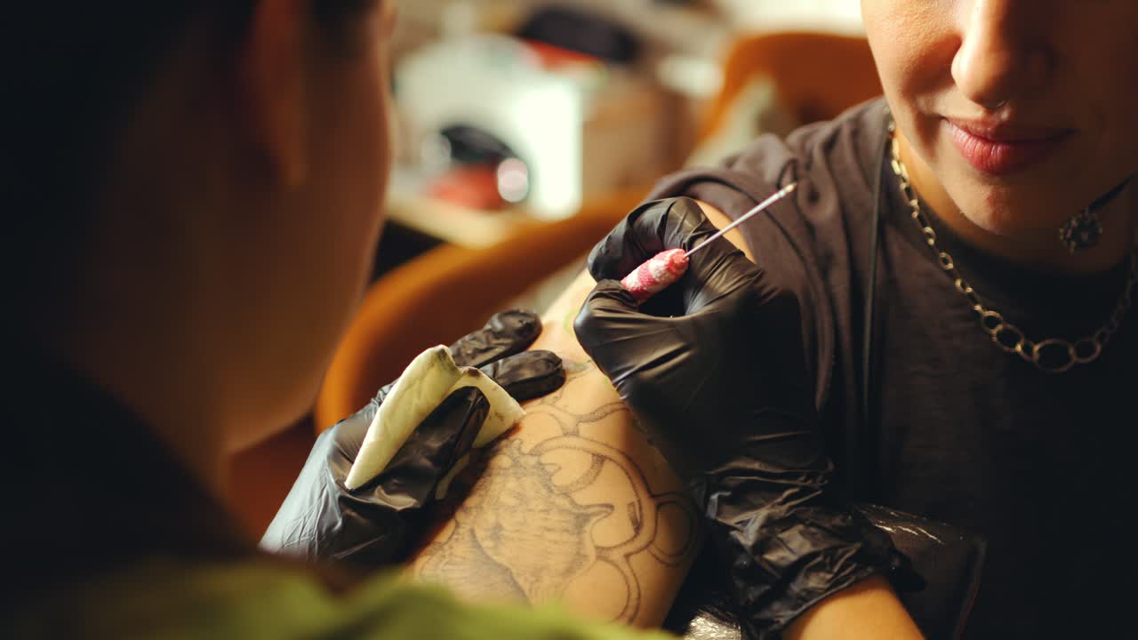 Primo piano di un artista che tatua la pelle sul braccio di una cliente con un ago