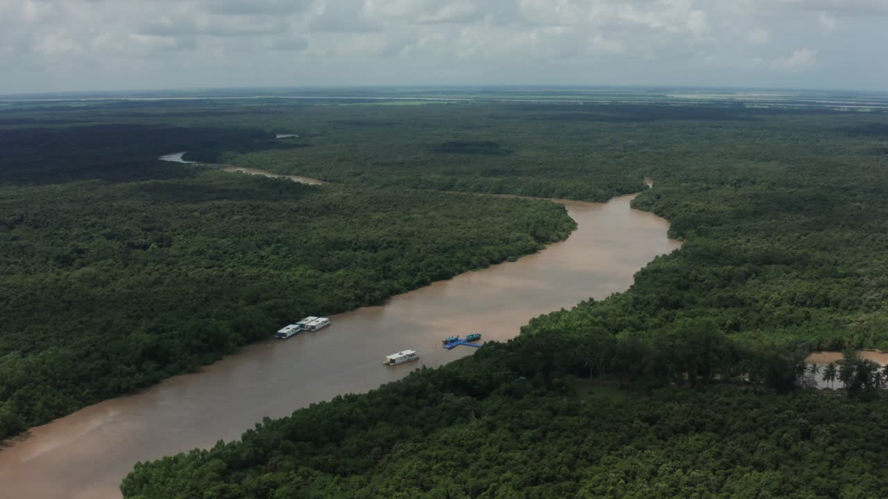 Um drone se afasta, revelando a imensa floresta de manguezais de Bhitarkanika, com rios lamacentos serpenteantes pontilhados por barcos de safári azuis em meio a um dossel verde infinito em Odisha, na Índia