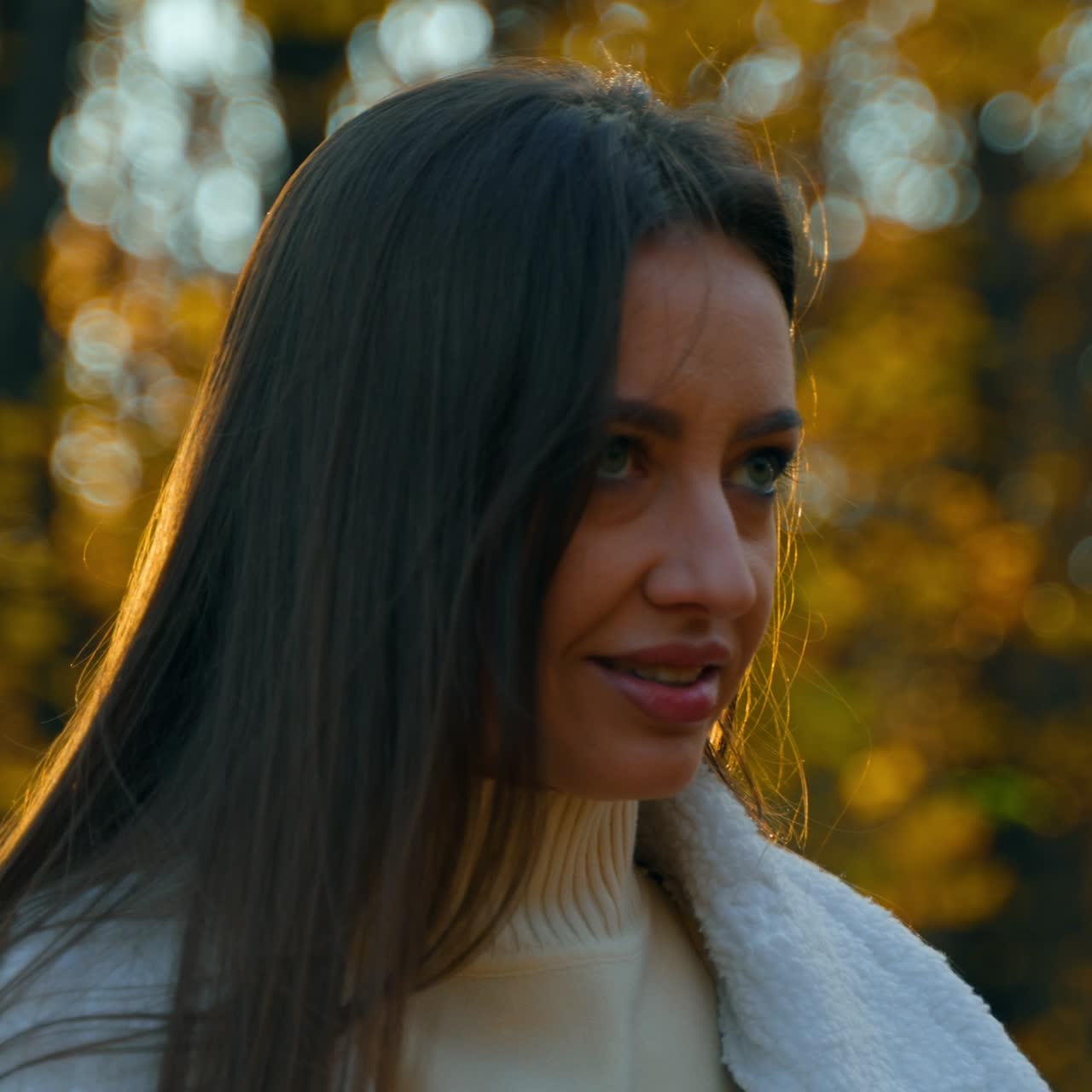 Romantic brunette walking by the autumn nature with a cup of coffee. Lady walks by the beautiful yellow-leaved park in the beams of sun