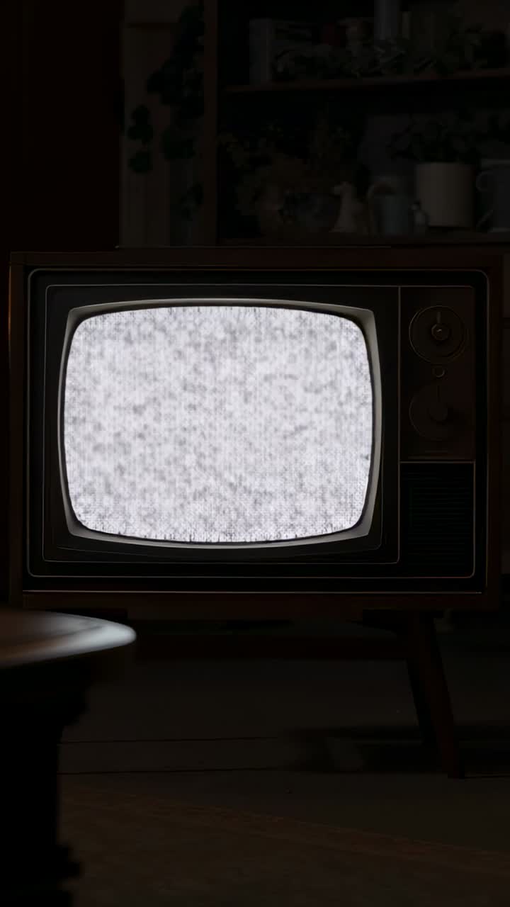 Video verticale: televisore CRT vintage su supporto che passa da luce bianca a statica nel soggiorno