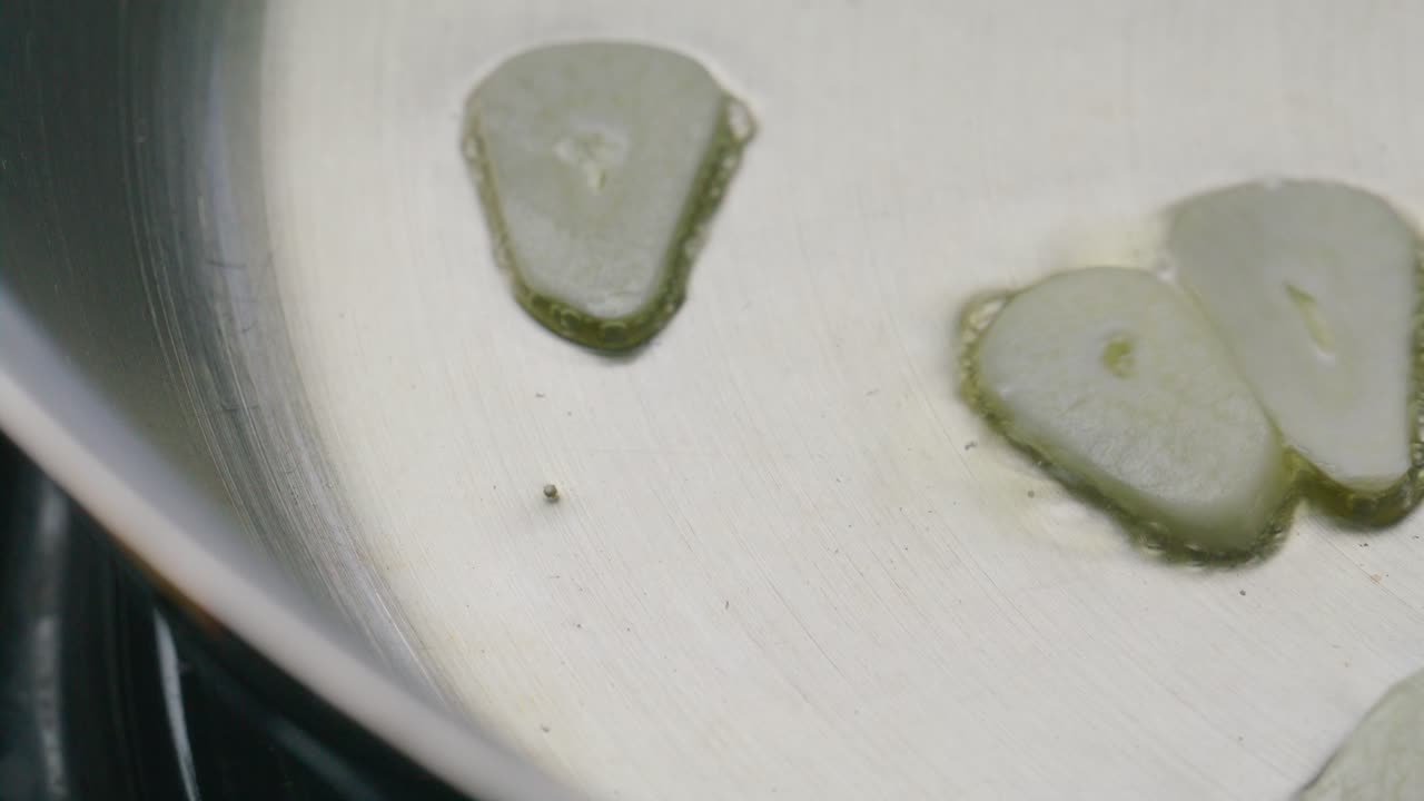 Chef Adding Slices of Garlic to Sizzling Oil in Frying Pan