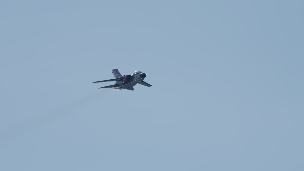 Militärjetplan flyger och svänger på klarblå himmel