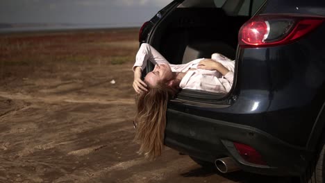 retrato de una viajera de cabello largo con un descanso en el maletero del coche y relajándose