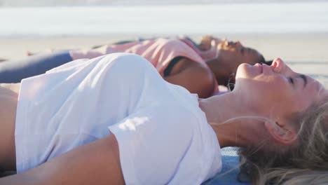 grupa różnorodnych przyjaciółek praktykujących jogę, leżących na maty na plaży