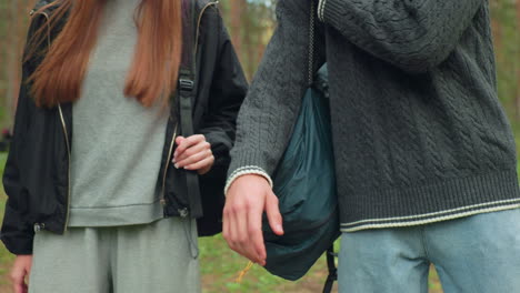 Close up of two friends stopping during stroll in forest, relaxed posture and expressive gestures indicating short pause from walk, surrounded by tall trees and natural greenery