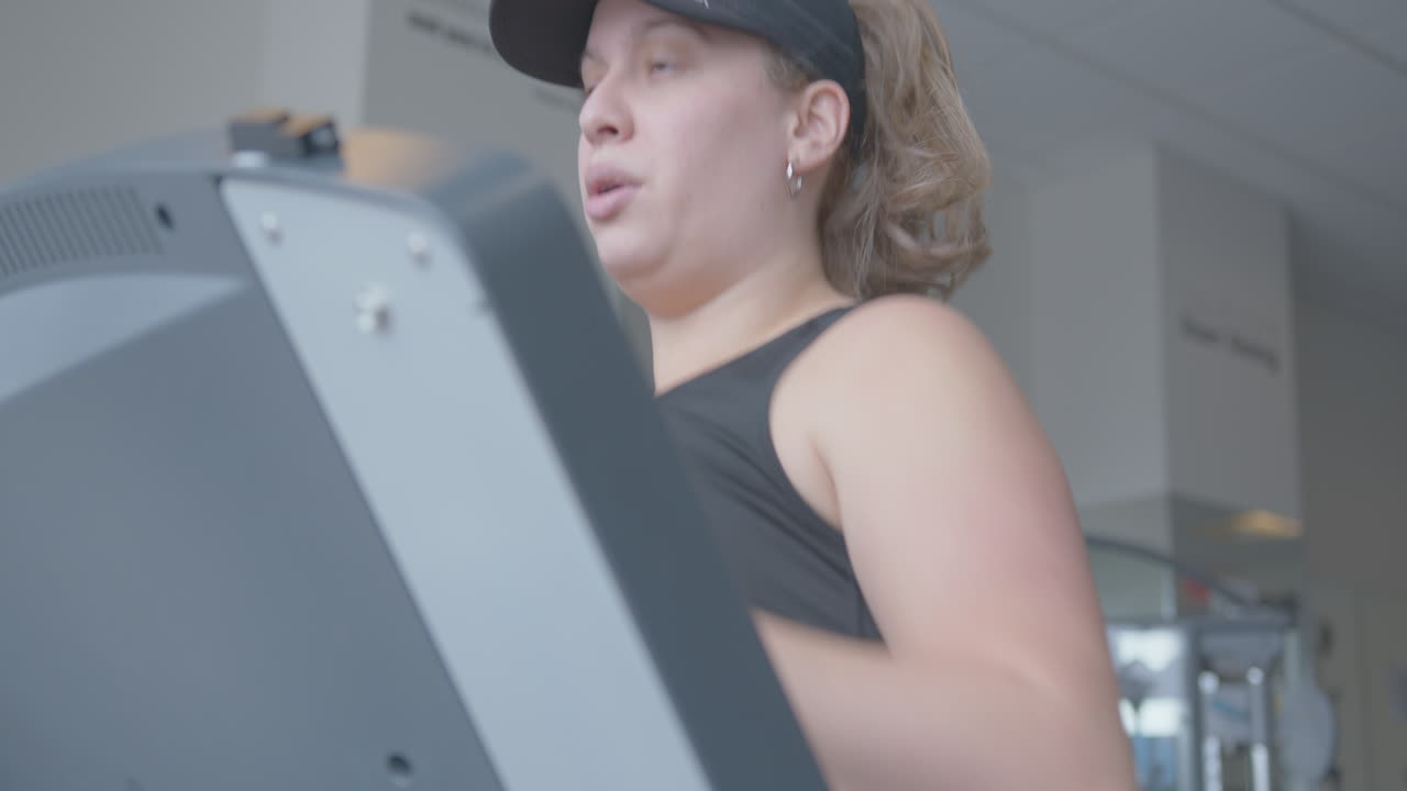 Primo piano con movimento della telecamera verso l'alto di un giovane che fa jogging su un tapis roulant.