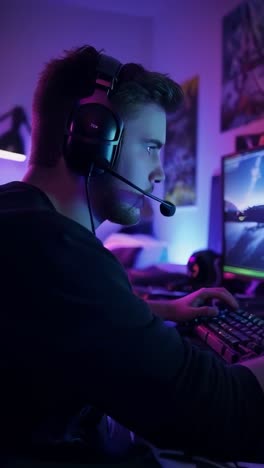 young gamer with headset playing video games in his bedroom, illuminated with neon lights.