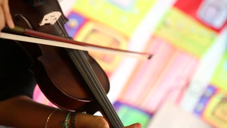 una mujer tocando el violín, una escena artística en la que se muestra el violín y una mujer lo sostiene y lo toca mientras filma una de las piezas dentro del colorido estudio de música