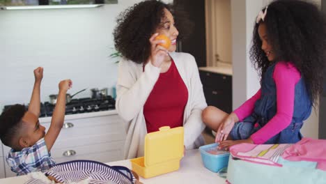 feliz madre afroamericana empacando caja de almuerzo para los niños a la escuela