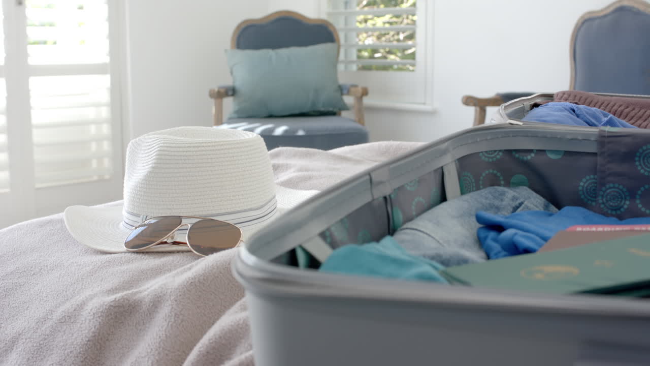 Close up of suitcase, hat and sunglasses on bed in bedroom, slow motion