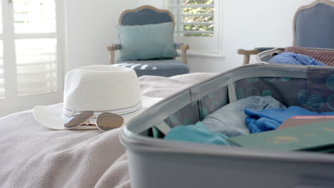 Close-up-of-suitcase,-hat-and-sunglasses-on-bed-in-bedroom,-slow-motion