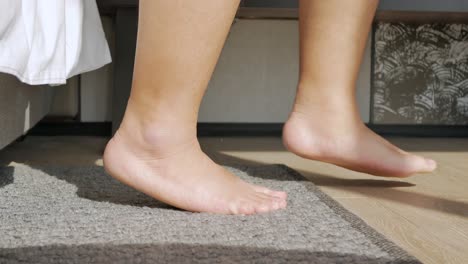 POV-to-feet-while-getting-out-of-bed,-steps-barefoot-on-the-floor-with-sunny-morning,-bed-room-vacation-holiday-time