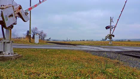 una vista de ángulo bajo de un antiguo tren de pasajeros de vapor que se acerca soplando vapor mientras las puertas de cruce bajan en un día de invierno