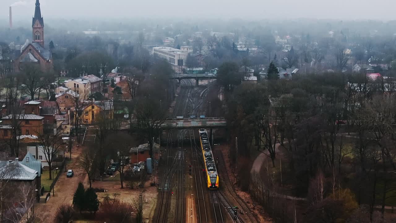 Yellow train leaving Riga, vehicles crossing small bridges in foggy winter mood