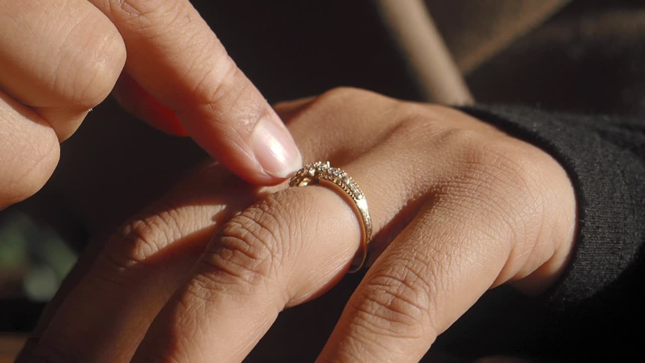 Primo piano di una mano che tocca un anello d'oro con diamante scintillante