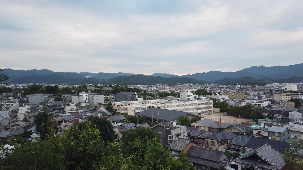 Panoramica aerea di un quartiere della città di Kyoto, Giappone, con scuola e campo sportivo, zona residenziale della tradizionale capitale giapponese con sfondo di skyline montuoso.