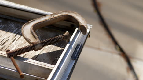 close up slide along a dirty plywood table with a rusty metal c clamp and vintage auto parts in an automotive scrap yard