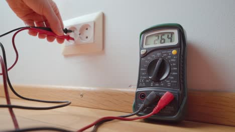 man measuring the voltage from a wall socket with a digital multimeter