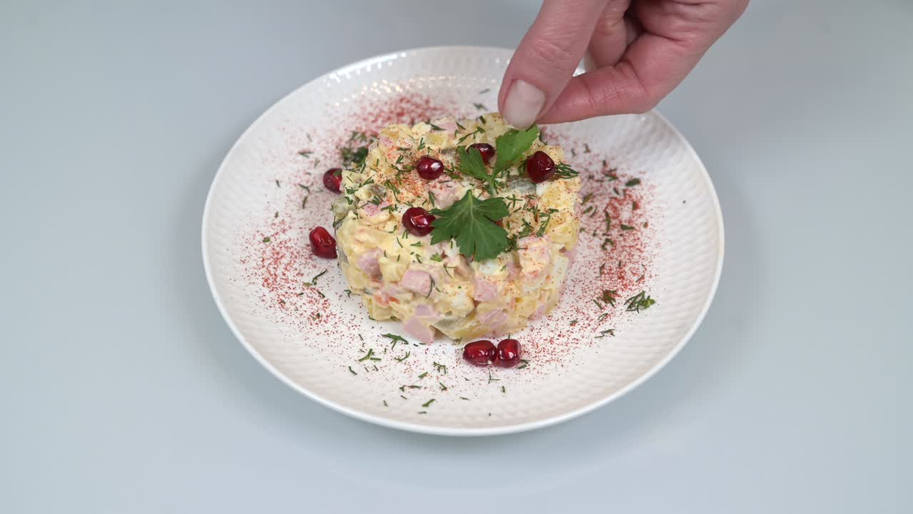 Woman's hand puts parsley leaves on served classic russian olivier salad