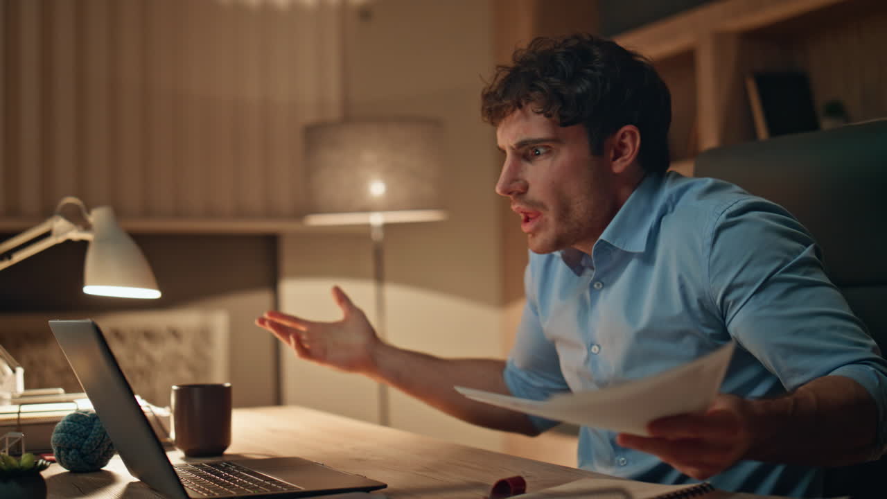 Investitore arrabbiato che parla in videoconferenza a tarda sera in ufficio, primo piano.