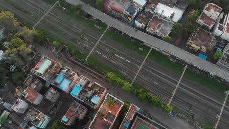 Railroad-tracks-in-T-Nagar,-Chennai-India,-cutting-through-the-city,-a-white-car-drives-on-a-road-beside-the-tracks