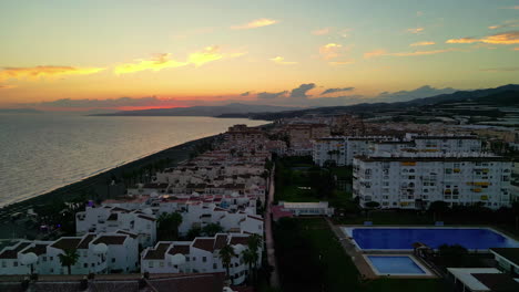 Toma-Aérea-Con-Plataforma-Rodante-Hacia-Atrás-De-La-Hermosa-E-Idílica-Ciudad-Española-De-Málaga,-Costa-Del-Sol,-Justo-En-La-Costa-Frente-Al-Mar-Tranquilo-Con-Edificios-Históricos-En-La-Hora-Dorada.