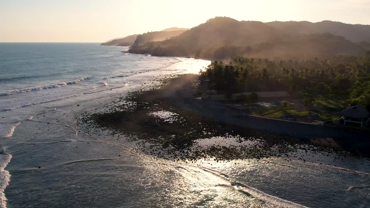 Volando sopra la costa e la scogliera, con le acque dell'Oceano Pacifico illuminate dai raggi del sole al tramonto.