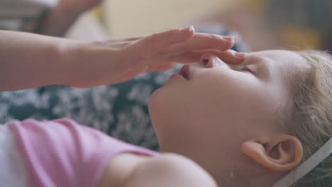 young mommy massages nose and forehead of girl on bed