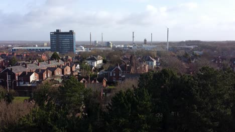 Aerial-view-over-park-trees-to-industrial-townscape-housing-with-Pilkingtons-blue-skyscraper,-Merseyside,-England