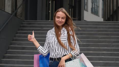 chica de moda sosteniendo bolsas de compras y mostrando los pulgares hacia arriba. regocijándose con buenos descuentos de ventas de vacaciones