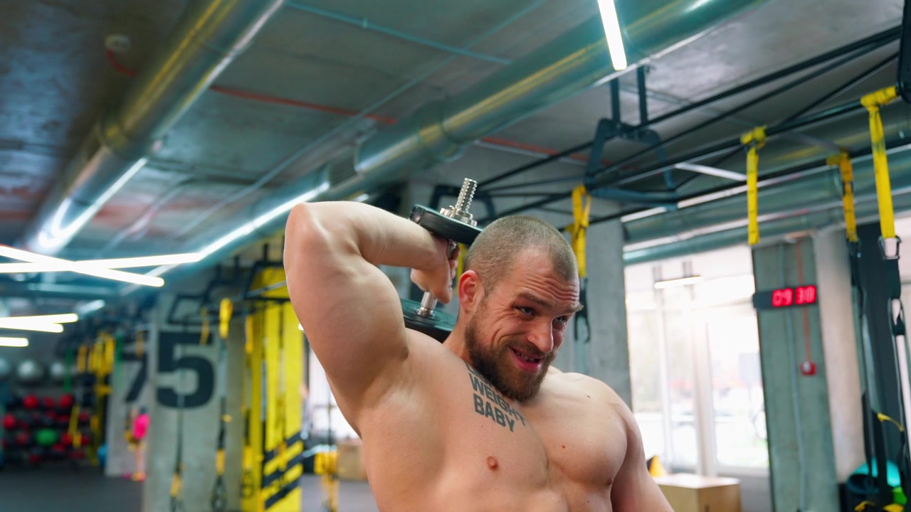 Uomo muscoloso che esegue estensioni con manubrio sopra la testa in una palestra moderna