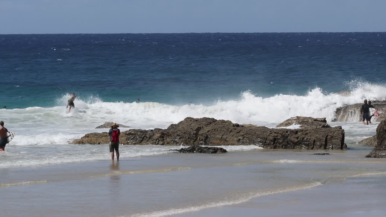 personas explorando una playa rocosa con olas estrelladas