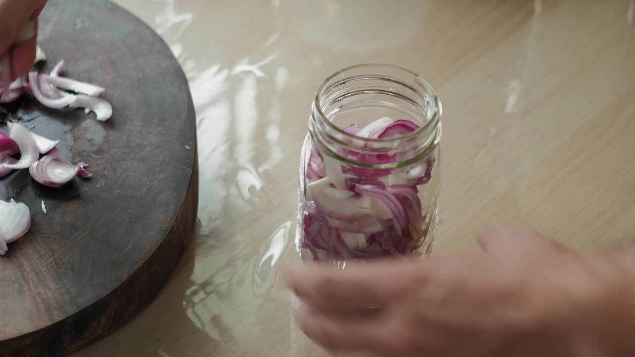 Hand Placing Chopped Red Onions Into Glass Jar In Kitchen. closeup shot