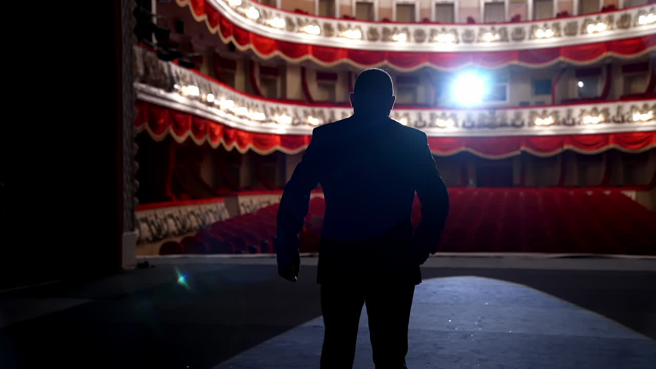 Actor on classic theatre stage. Man is speaking in spotlights during the performance. Back view video.