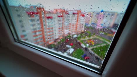 view through the window on raining weather. drops of rain on a window pane on the city buildings background. rain droplets flowing on a glass.