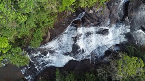 drone with camera down making slow upward movement of a beautiful waterfall, flowing waters and exuberant nature around