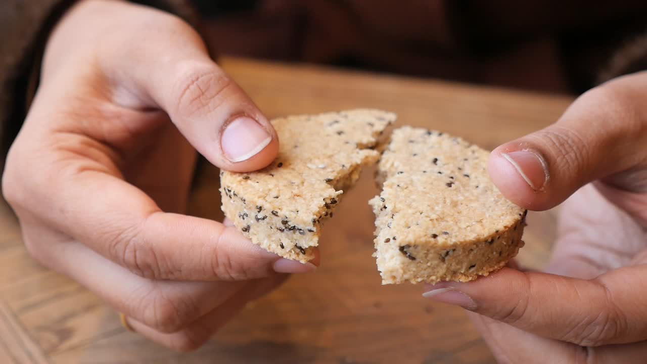 Close-up of Hands Breaking a Crumbly Cookie with Chia Seeds