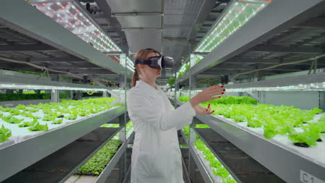 una mujer microbióloga moderna usa gafas de realidad virtual para controlar y controlar el clima en una granja moderna para cultivar verduras ecológicas.