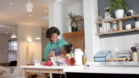 happy african american mother and daughter preparing dough in bowl in kitchen, slow motion