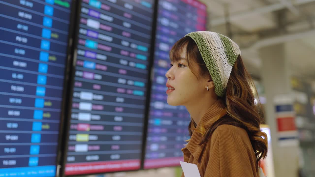 4K Asian woman checking timetable flight schedule in airport terminal.