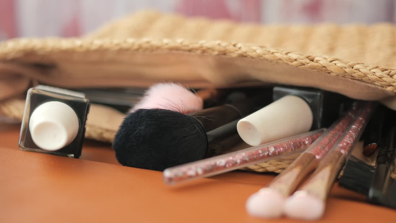 Close-up of makeup products and brushes spilling from a straw bag