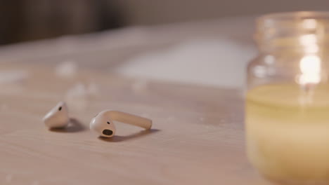 close up view of earphones and a candle on top of a wooden table, in the background a blurred bathtub filled with water and foam